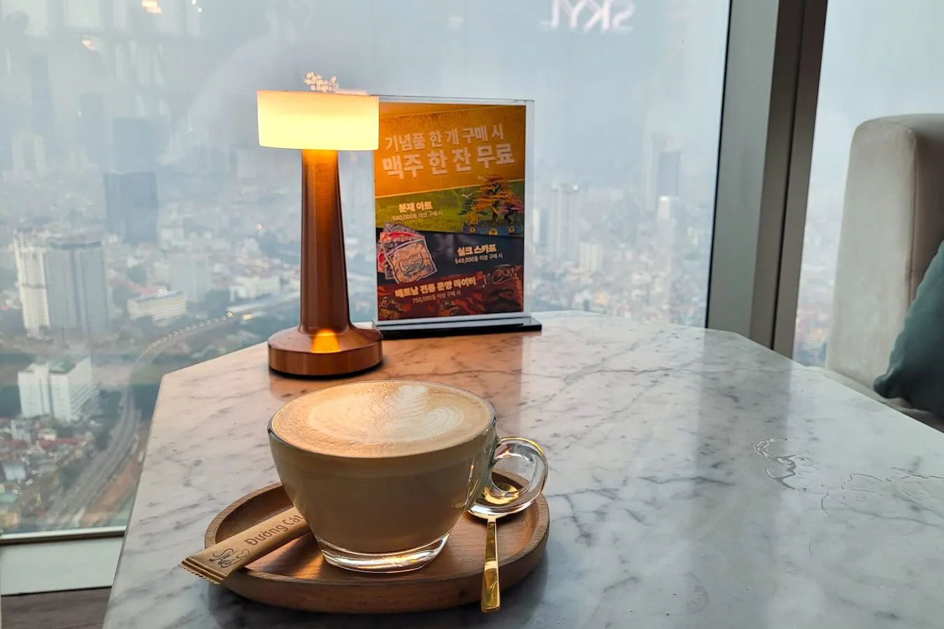 Cappuccino on a marble table by the window at the SKYL lounge, Hanoi below